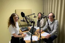 Three persons are standing in a studio, recording a podcast