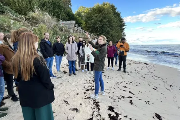 A group of people standing on the beach, listening to a teacher speaking