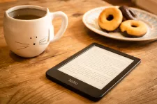 A cup of tea, a tablet and three donuts. Photo.