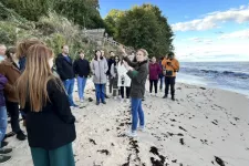 A group of people standing on the beach, listening to a teacher speaking